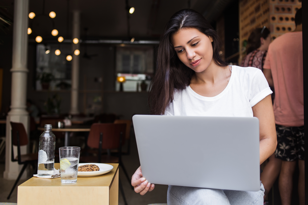 Hispanic woman at café with laptop taking a business online course, representing "cursos de negocios en línea"