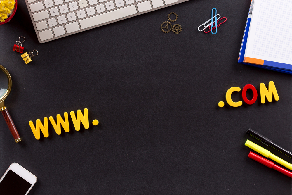 Letras "www.com" sobre escritorio con computadora y celular, para ilustrar la idea de "construye un sitio web para tu empresa"