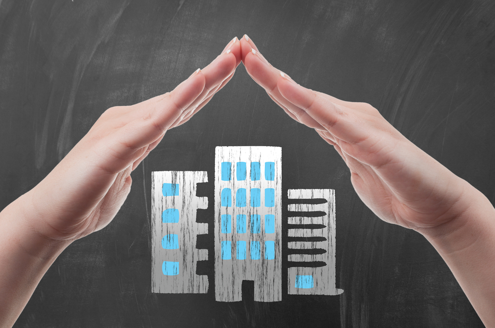 Hands protecting business buildings to illustrate the concept of business protection