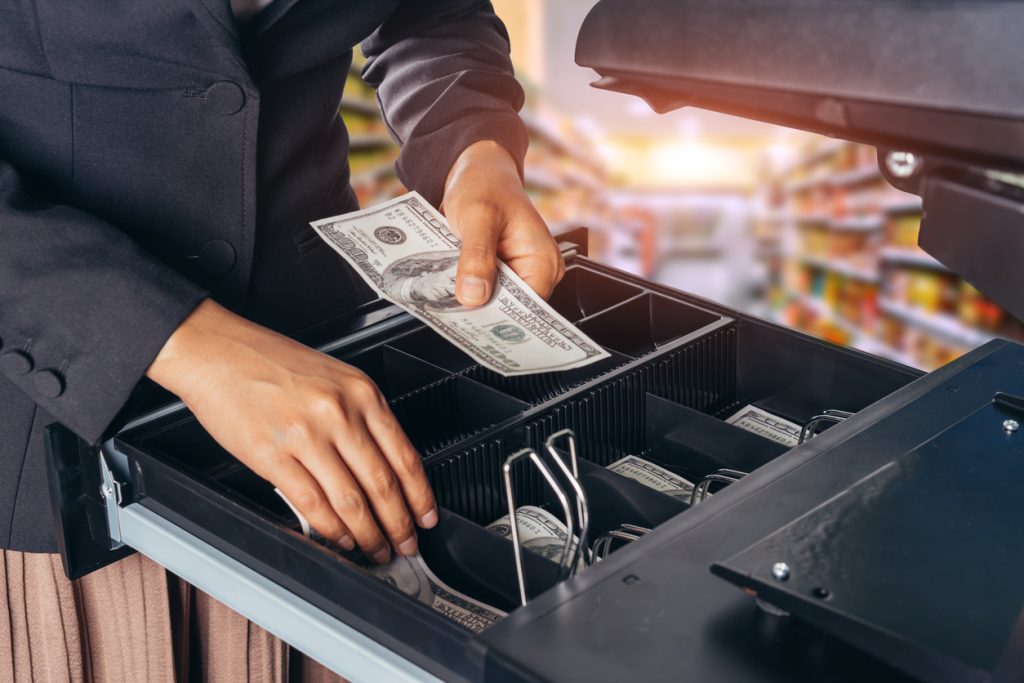 Mano de mujer depositando billetes en caja registradora. Concepto: Cómo calcular el flujo de caja libre de tu empresa - Fórmula de flujo de caja libre