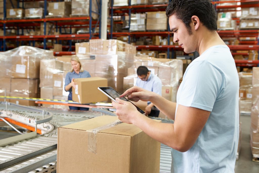 Worker Using Tablet Computer In Distribution Warehouse Looking At Notes. Concept: cost of sales