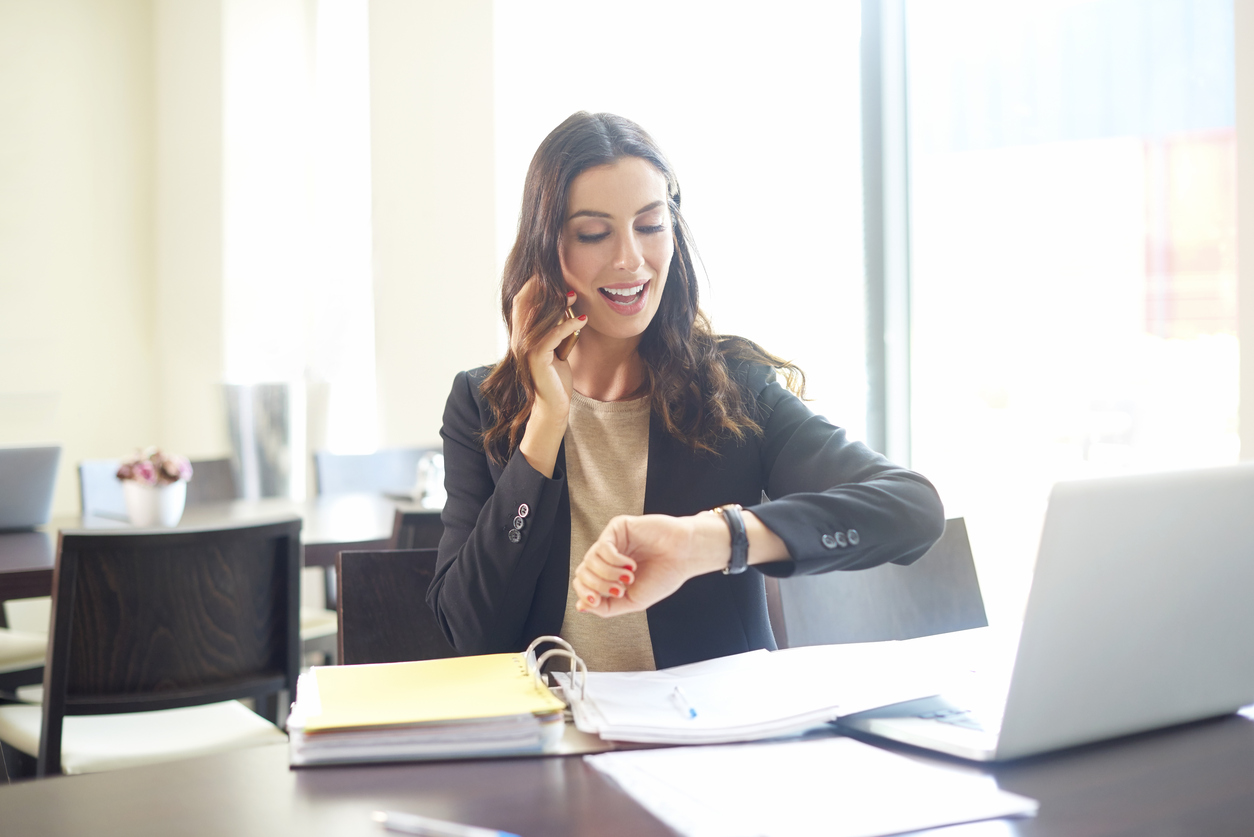 Business woman on her desk talking on her cellphone and checking her watch, to illustrate the idea "time management"
