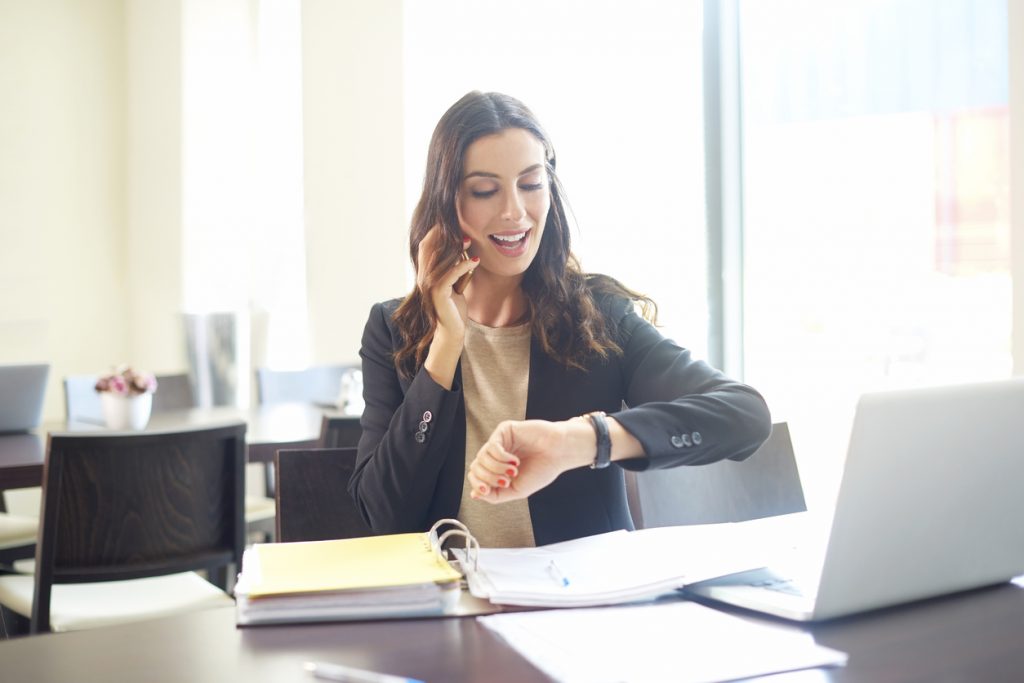 Mujer de negocios hablando por celular y mirando su reloj para expresar la idea "gestión de tiempo"