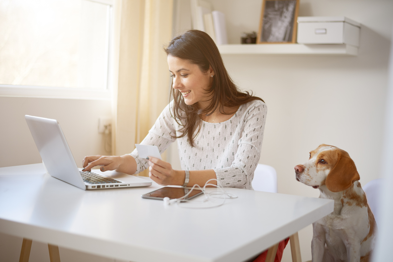Woman at her home desk using laptop with dog next to her, to illutsrtae the idea "home business".