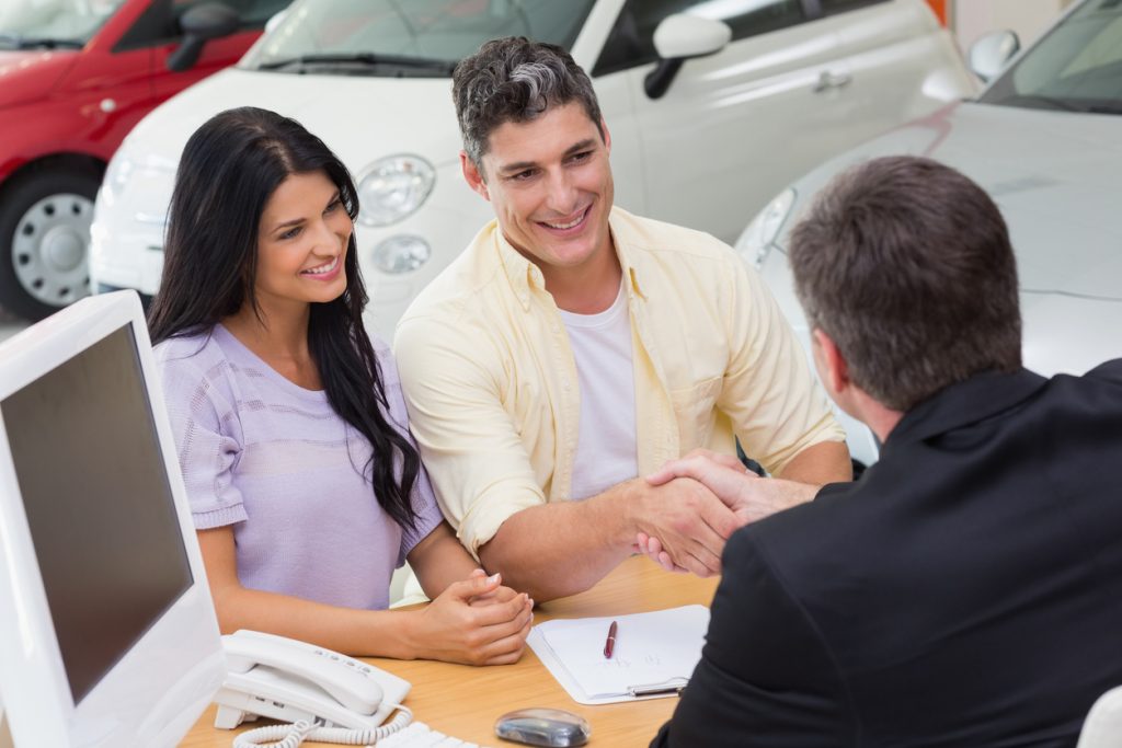 Smiling salesman shaking a customer hand at new car showroom to show concept of "sales funnel"
