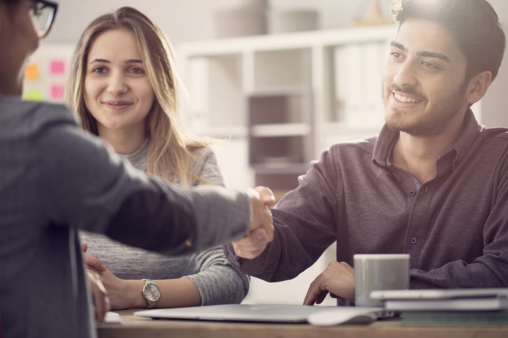 Young couple at bank shaking hands with a female representative and closing a dealto ilustrate the idea "How much can I borrow for my business?"