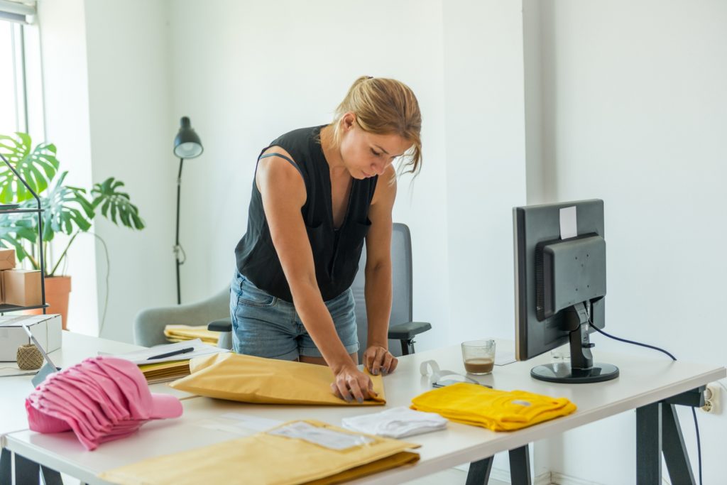 Mujer trabajando en casa empaquetando ropa en sobres para enviar, para mostrar cómo ganar dinero en línea