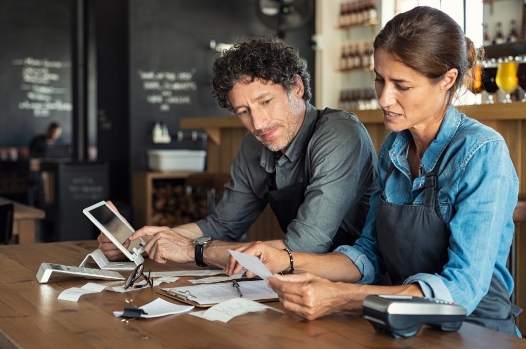Couple of restaurant business owners sitting in cafeteria discussing finances, doing paperwork, and discussing options for a business bank account