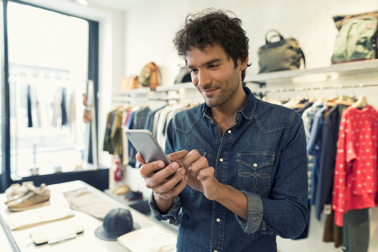 Business owner using smart phone in clothing store. Concept: online bank account.