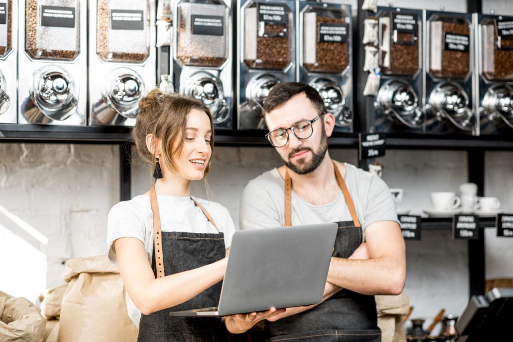 Pareja de dueños de tienda de café en el mostrador, leyendo en un laptop. Concepto: cómo leer tu reporte de credito.