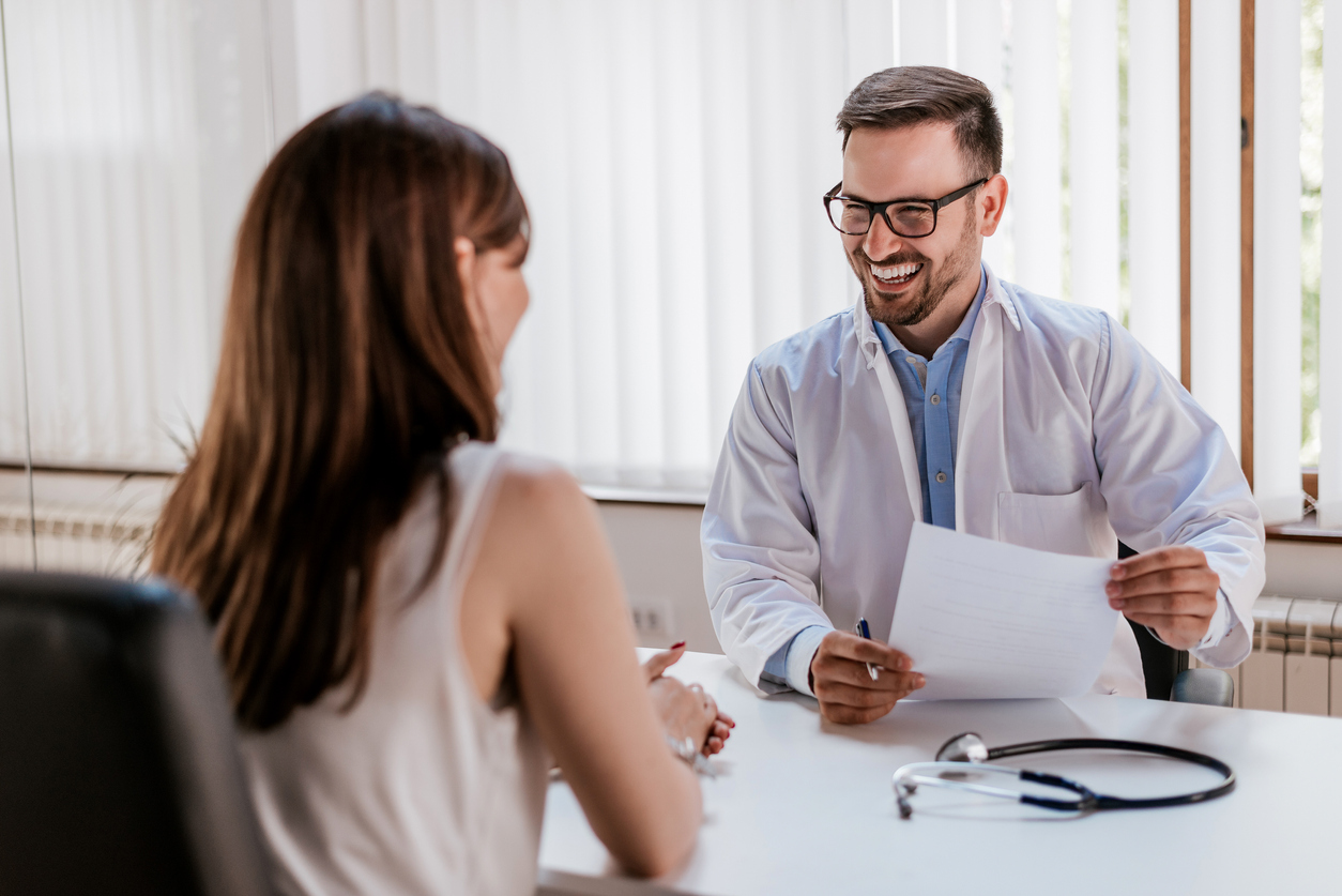 Happy male doctor discussing with patient at table in clinic. Concept: healt insurance options