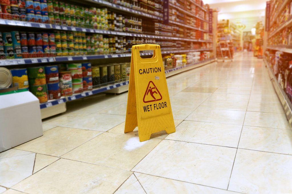 Yellow sign - caution. Wet floor is in the supermarket against the background of blurry products standing on the shelves. Concept: business lawsuit.