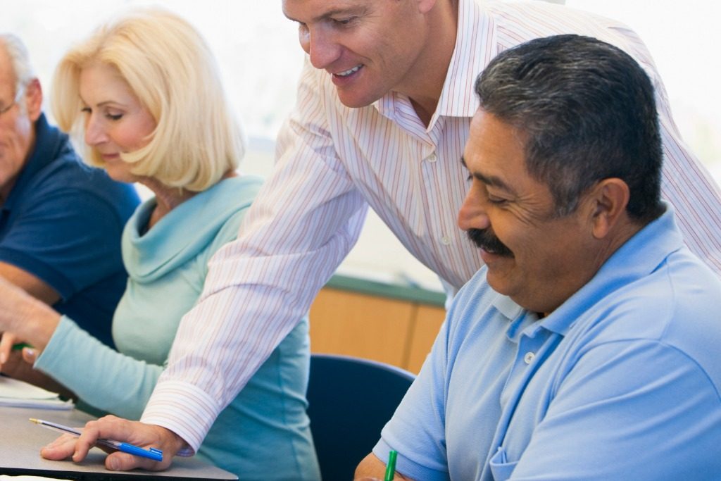 Teacher in class assisting a male Hispanic adult student. Concept:Immigration help: education in finances