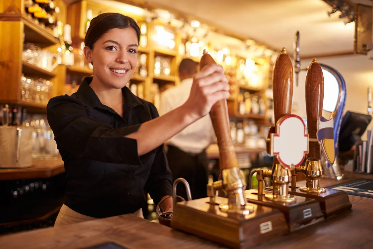 Una joven mujer trabajando detrás de un bar mirando un la cámara