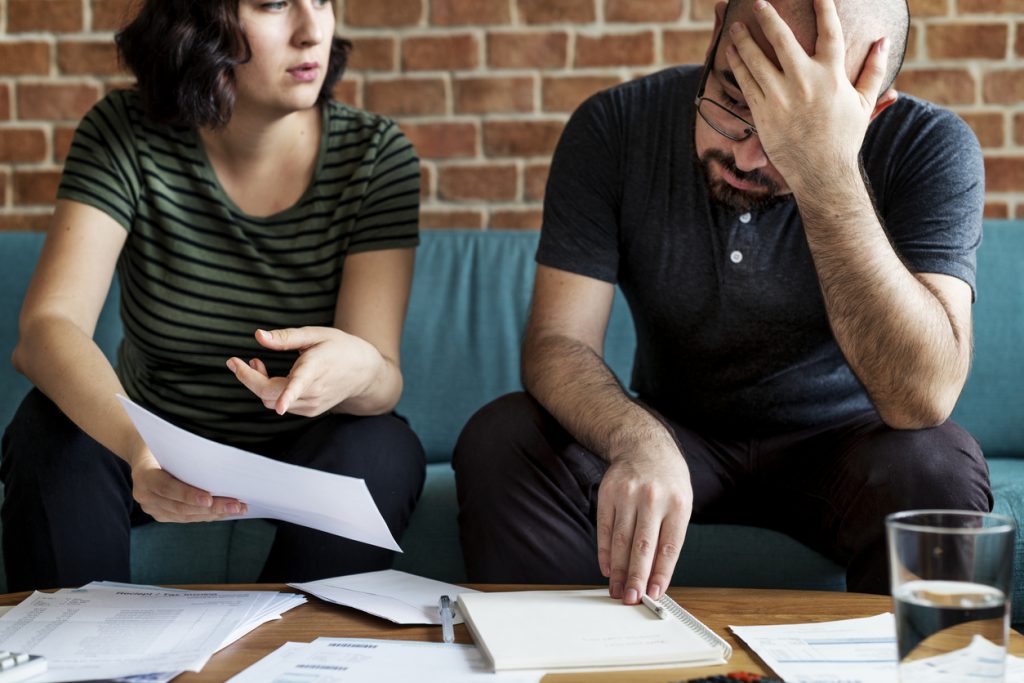 Worried couple on couch with paperwork managing debt. Concept: pay off debt