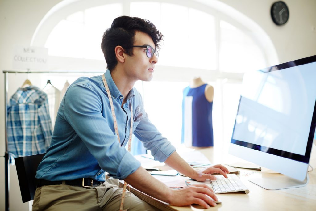 Young creative fashion designer sitting in front of computer and searching in the net. Concept: business loan refinancing