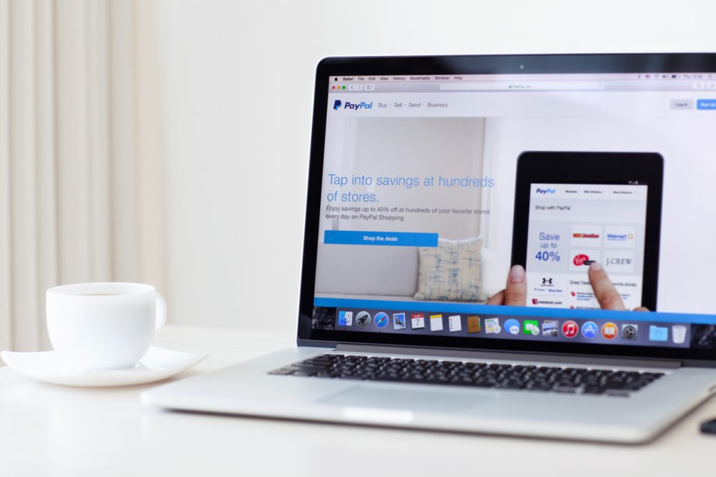 Laptop sobre escritorio mostrando página principal de PayPal. Concepto: cómo usar PayPal en tu negocio