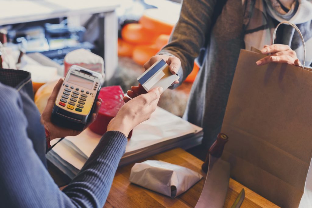Cliente pagando en tienda de comestibles con tarjeta de crédito; dependiente usando lector de tarjeta de crédito. Concepto: adelantos de efectivo.