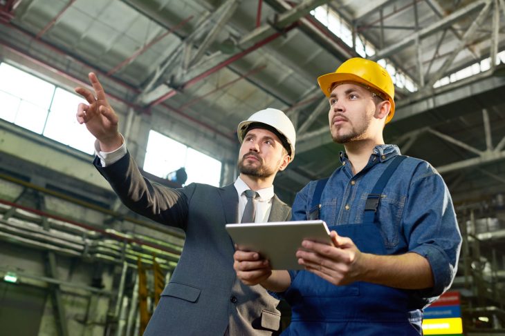 Businessman pointing up while discussing some future plans with factory worker holding digital tablet. Concept: how much to invest