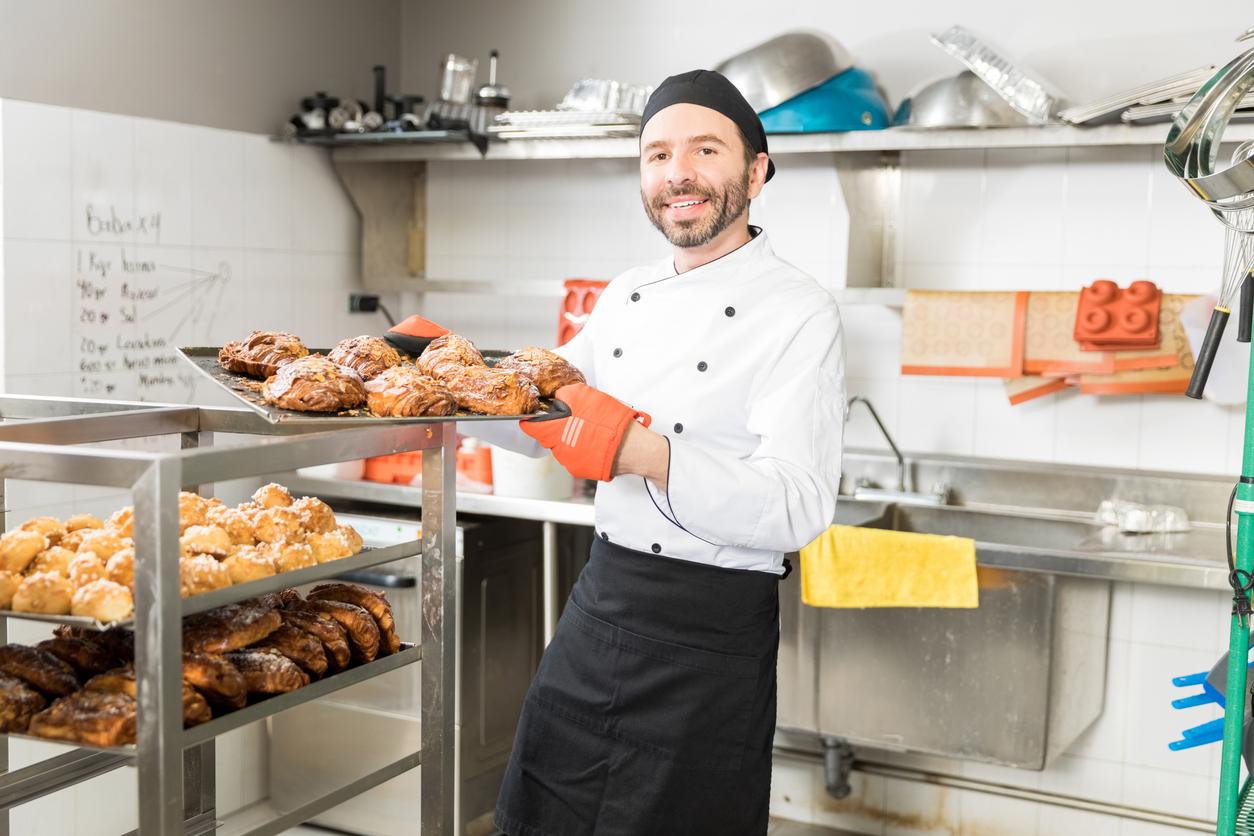Smiling small business owner (baker) showing yummy pastries in professional kitchen. Concept: microloan