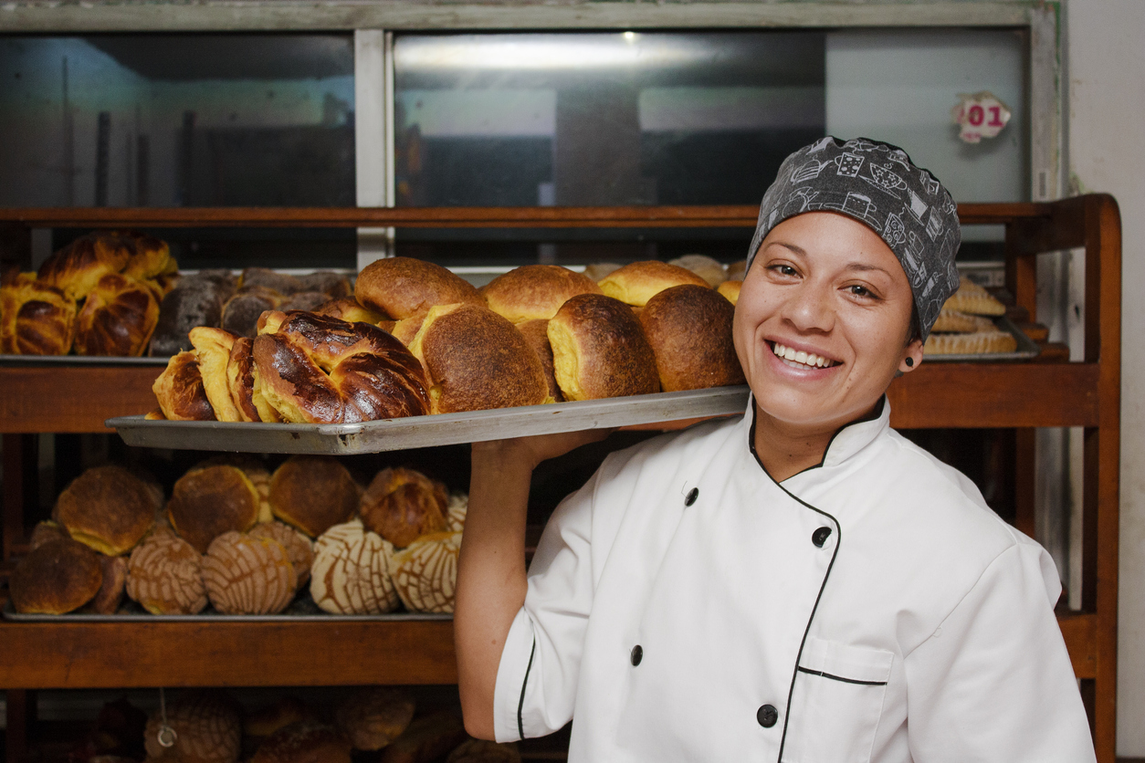 Smiling immigrant business owner (bakery) carrying a tray of fresh baked goods. Concept: loans for immigrants