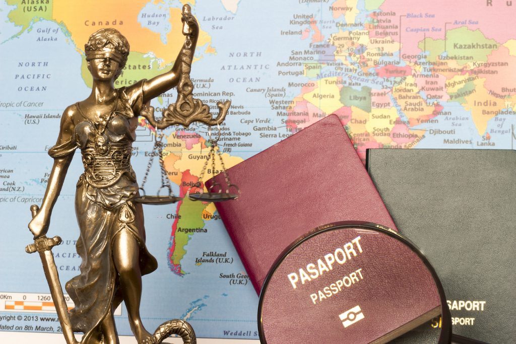 Estatua de la justicia, pasaportrs y lupa con fonde de mapa mundial. Concepto: ayuda para inmigrantes: recursos legales