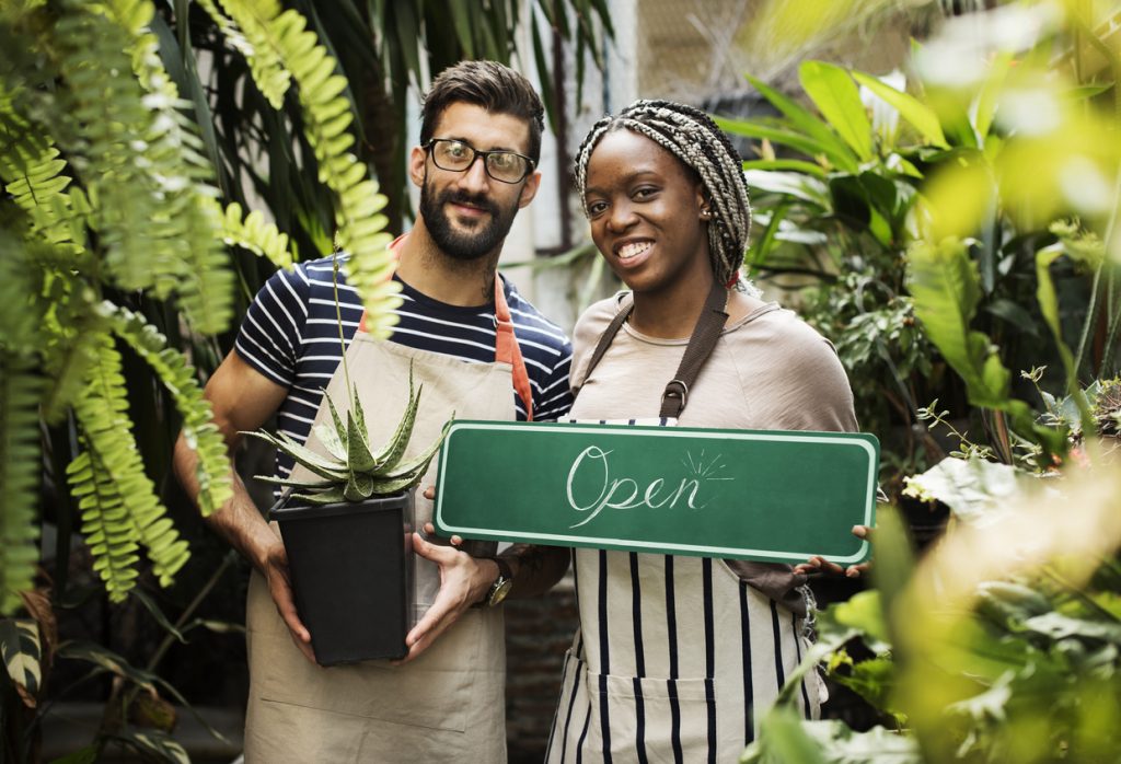 Couple of business owners at flower shop holding an "open" sign. Concept: how to change your business name.
