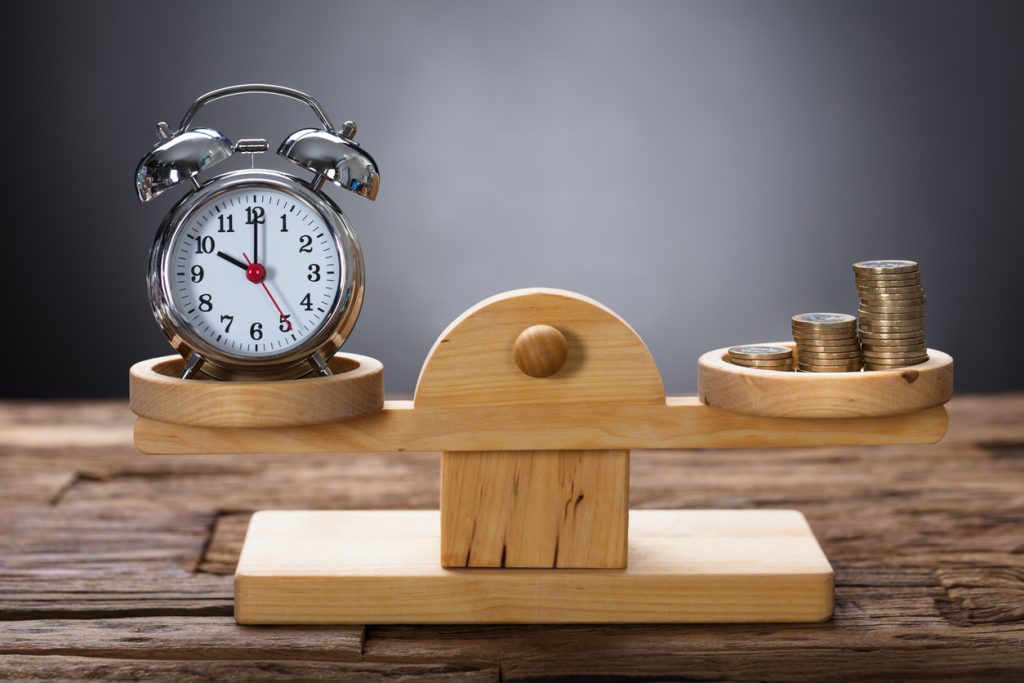 Closeup of clock and coins balancing on wooden weighing scale representing cash flow vs profit concept