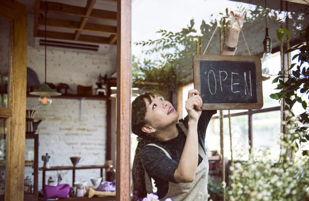 Young female entrepreneur hanging an open sign in small business. Concept: how to start a business with no money