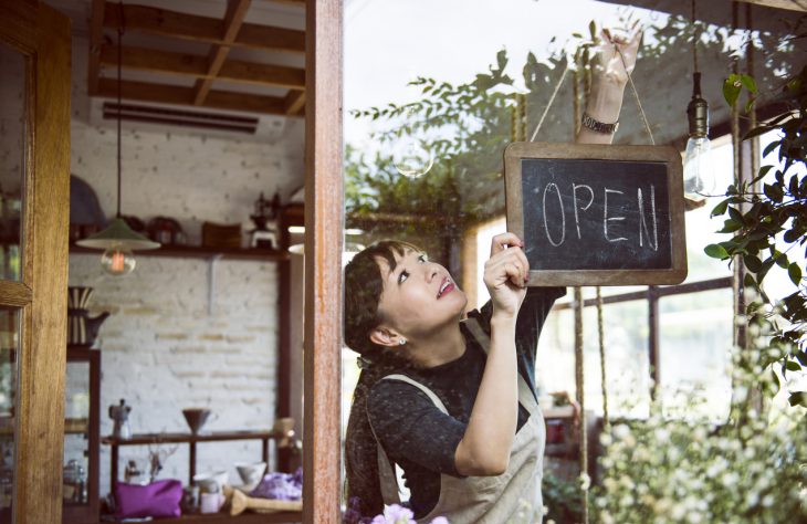 Young female entrepreneur hanging an open sign in small business. Concept: how to start a business with no money