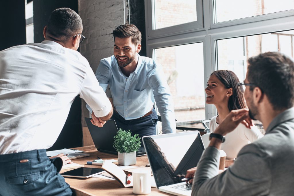 Young business owner and client in smart casual wear shaking hands and smiling while working in the office. Concept: How to negotiate a contract.