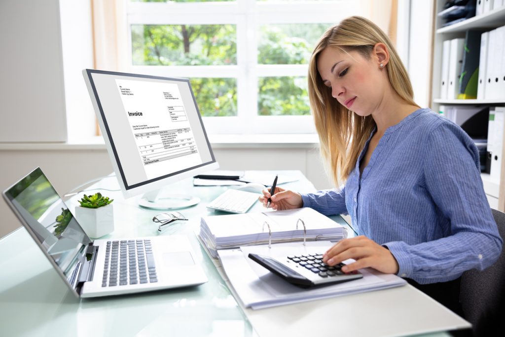 Young Business owner writing invoice With Computer And Laptop On Desk. Concept: invoice payment terms