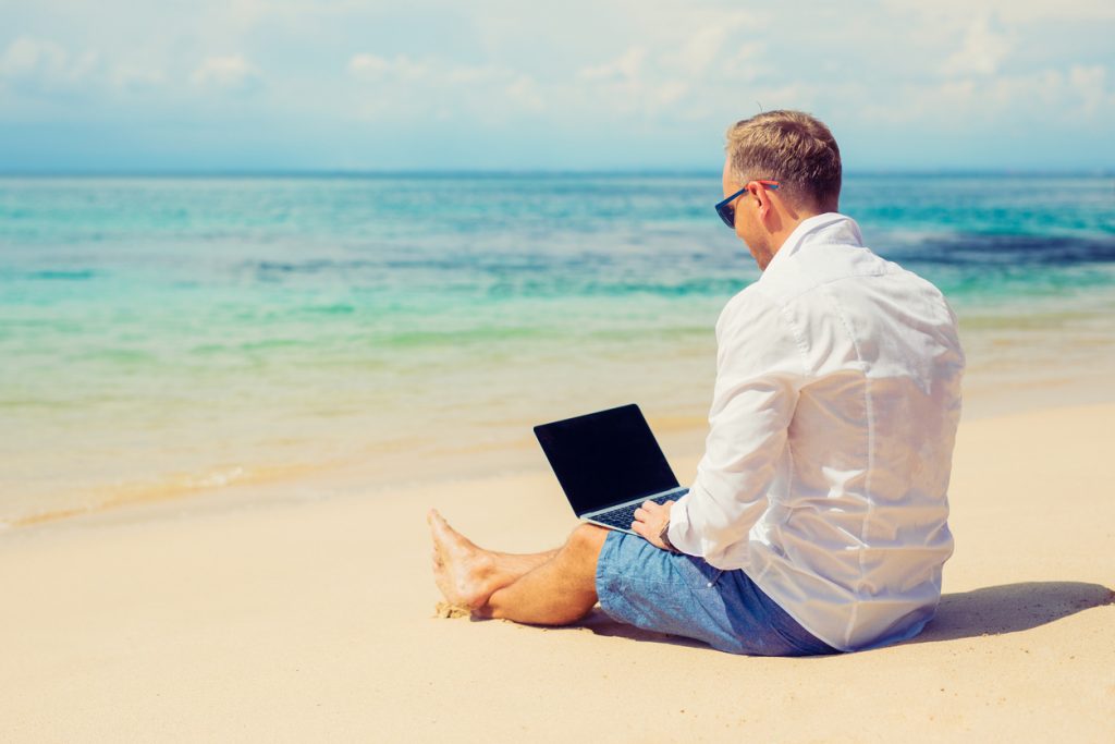 Empresario joven usando computadora en la playa en el verano. Concept: Ideas para negocios de verano