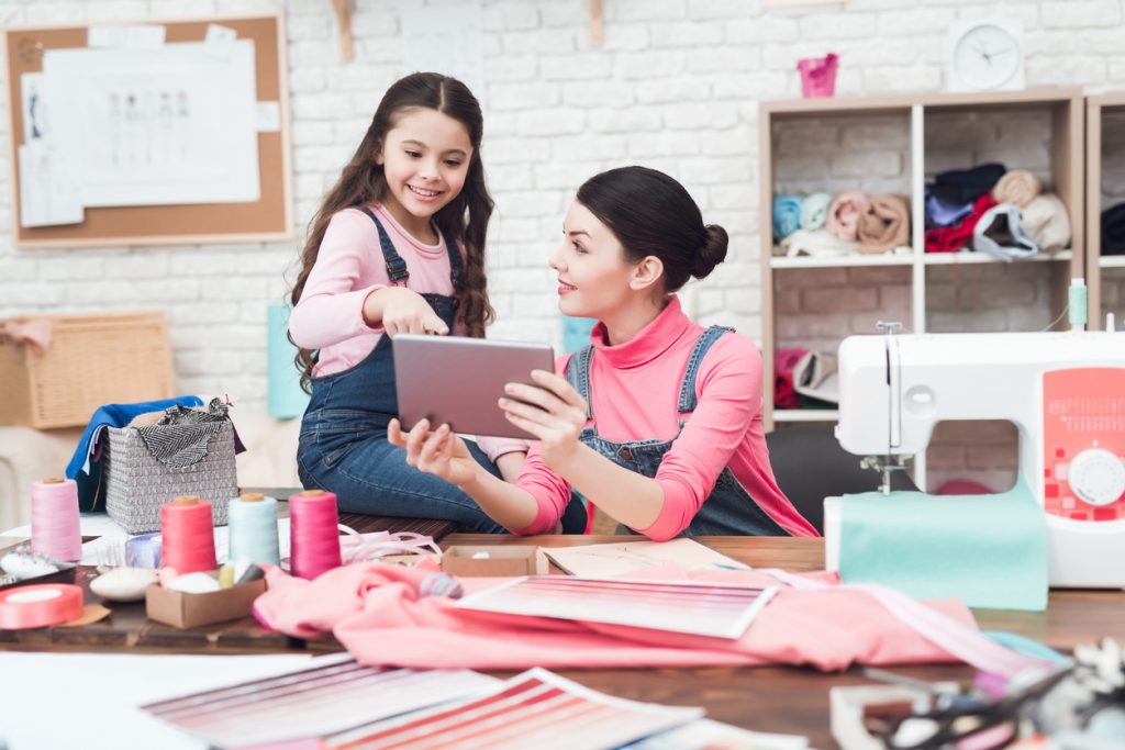 Mompreneur and daughter looking at tablet in a sewing workshop. Concept: mompreneur