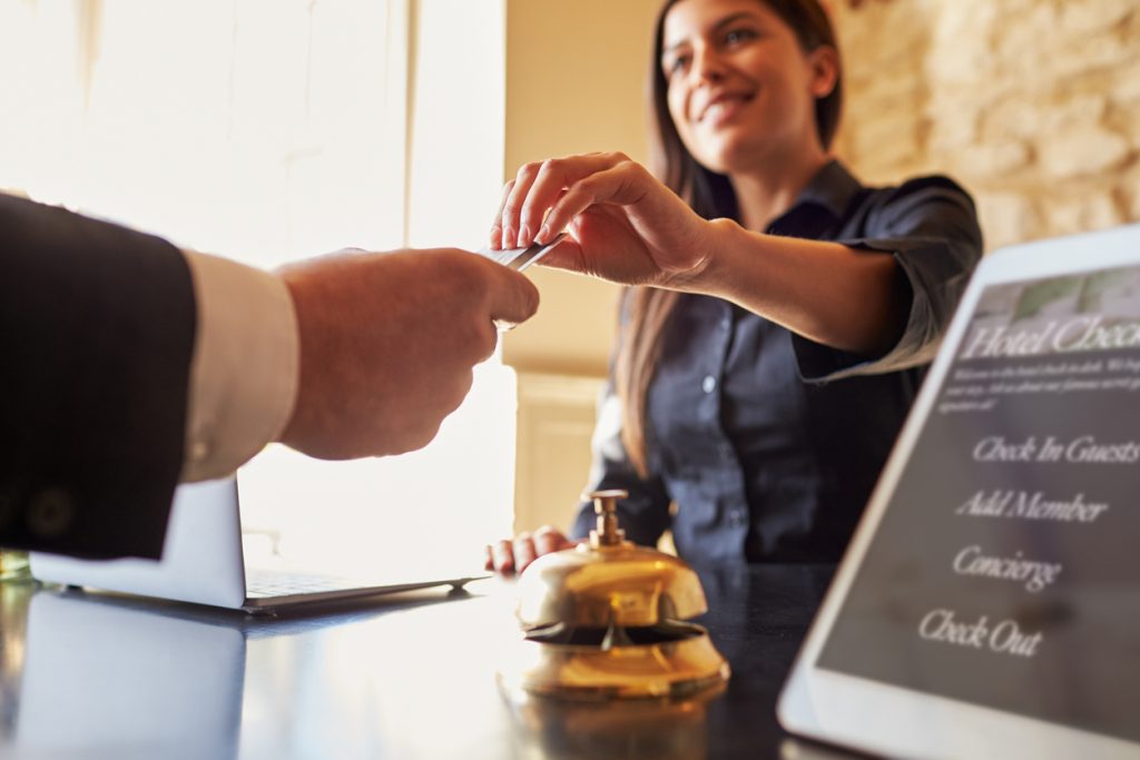 Guest takes room key card at check-in desk of hotel, close up. Concept: how to get a business loan for your hospitality business