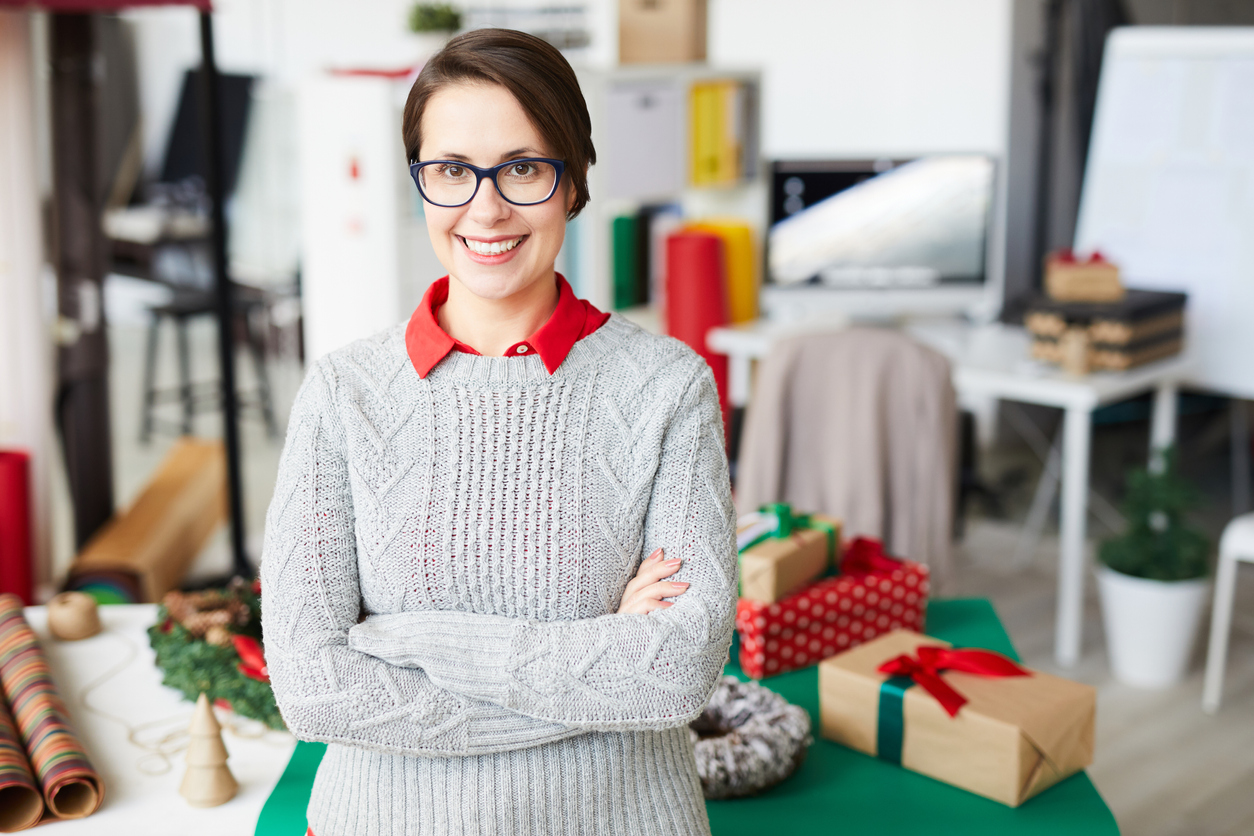 Young smiling businesswoman in studio with packages in the background during winter season. Concept: Low season survival of your small business