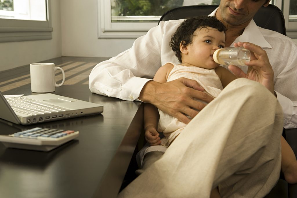 Padre alimentando a su bebé en la oficina. Concept: Logra un balance perfecto entre la paternidad y los negocios