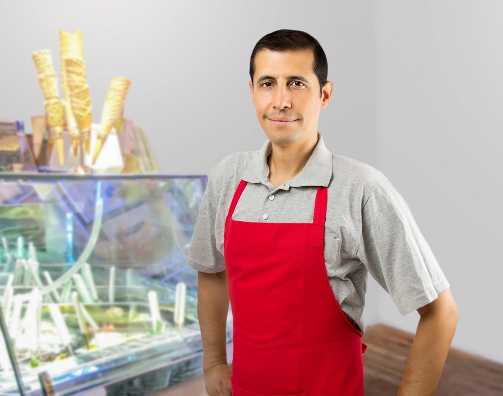 Smiling ice cream store employee standing behind the counter in the store. Concept: Seasonal businesses problems and solutions