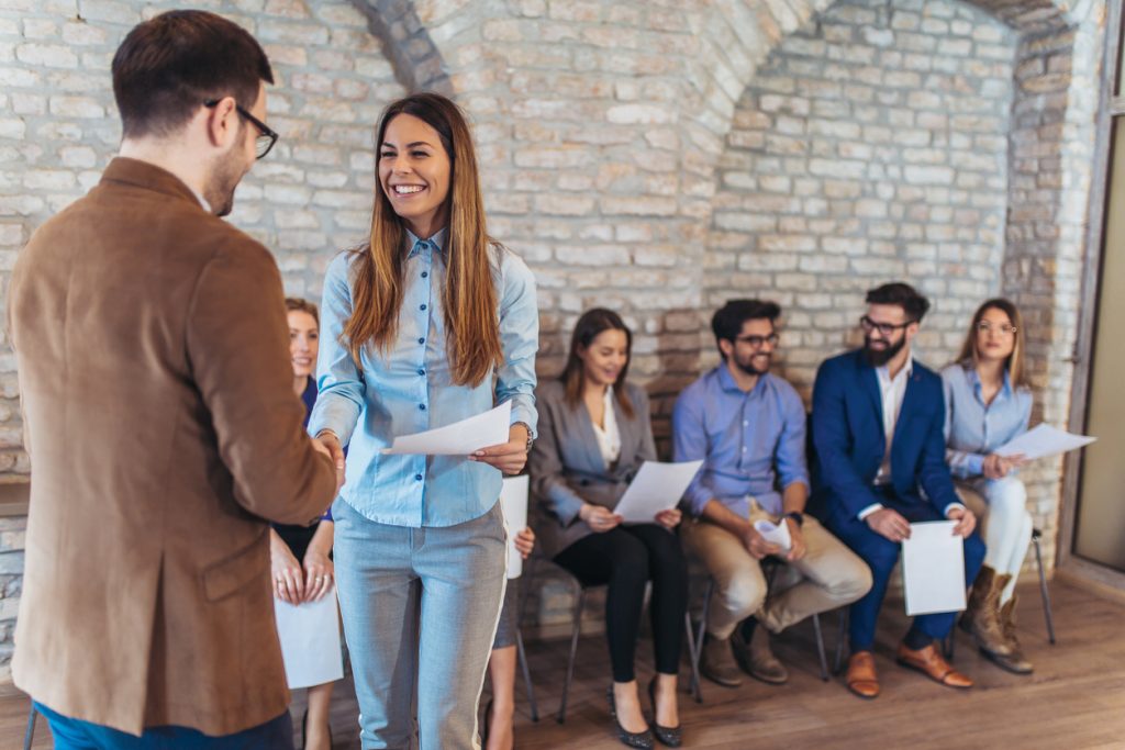 Hombre en oficina dandole la mano a una chica lista para su entrevista en una oficina moderna. Concept: Cómo contratar estudiantes para tu pequeña empresa