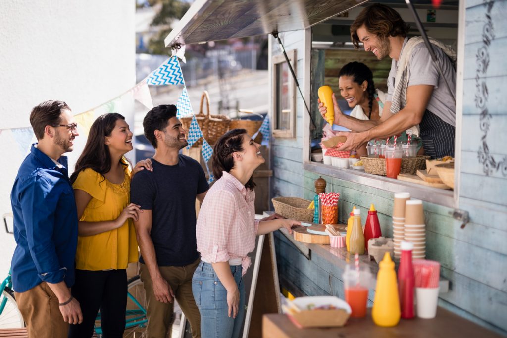 Smiling waiter giving order to customers at counter in food truck van. Concept: how to expand your food truck business