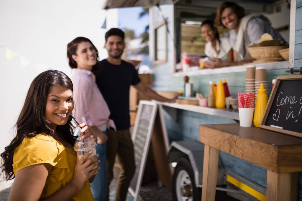 Retrato de amigos sonriendo mientras compran comida en un food truck. Concept: cómo empezar un food truck para expandir tu restaurante