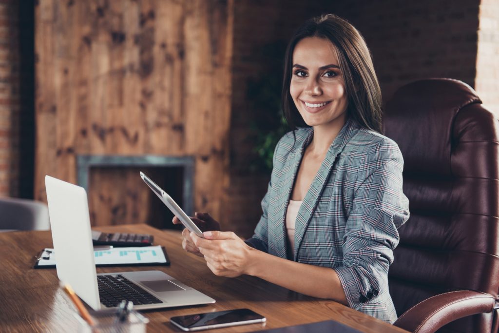 Profile side view photo of intelligent stylish boss in a gray checkered jacket sitting in office chair in workstation on industrial style half a turn with a tablet in hand. Concept: wosb