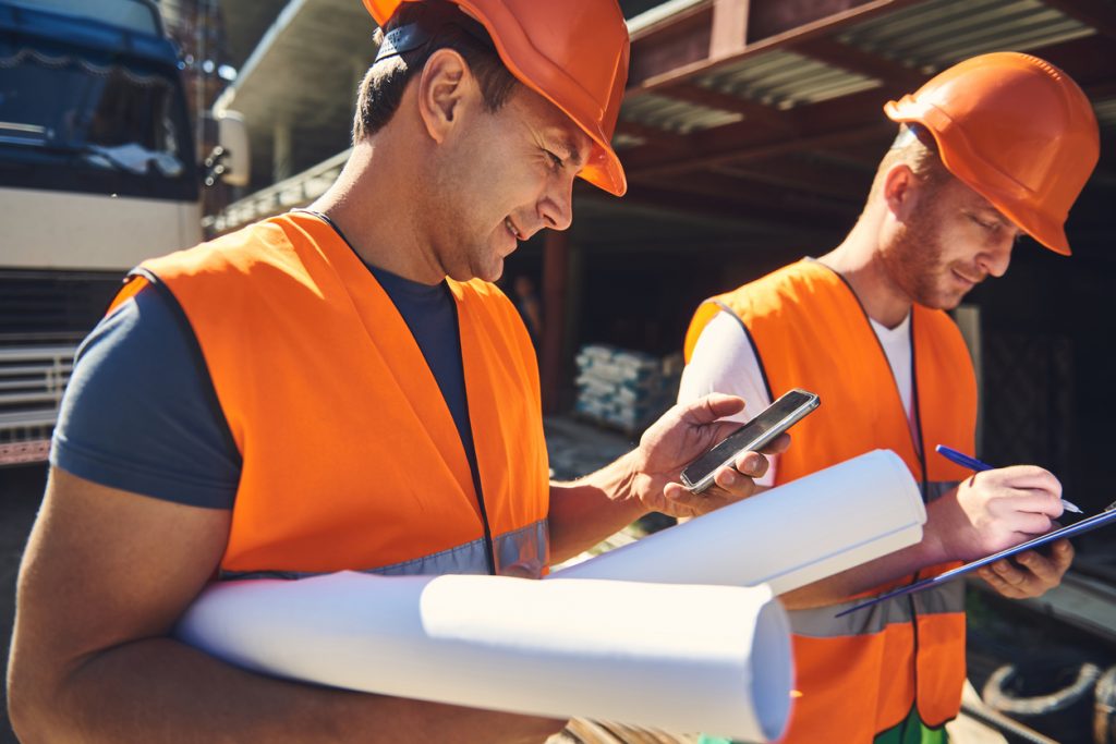 Two construction workers in construction site with blueprints and cellphone. Concept: Store credit cards for construction companies
