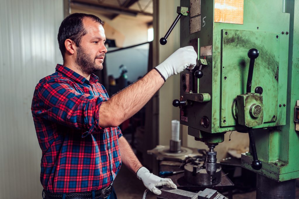 Worker using drill press in factory. Concept: Trump import tariffs