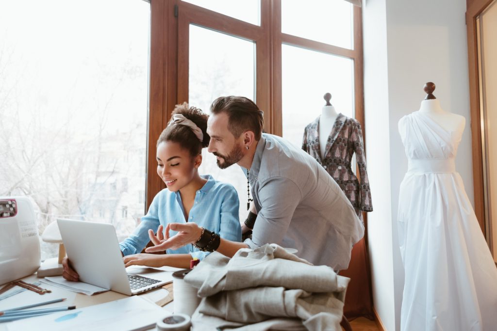 Man and woman looking at laptop in bridal dress design studio.