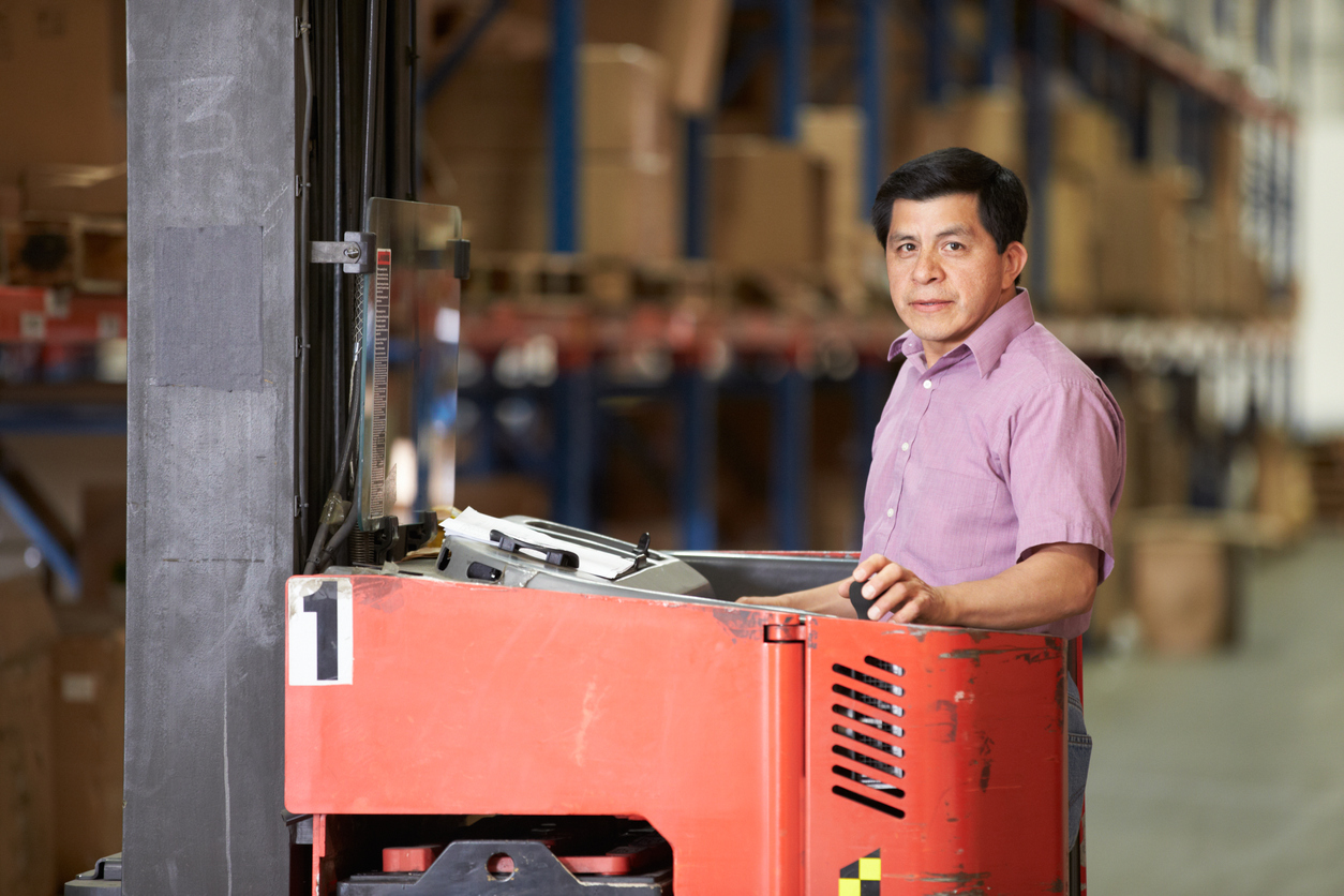 Immigrant worker driving Fork Lift Truck In Warehouse. Concept: immigration and small business