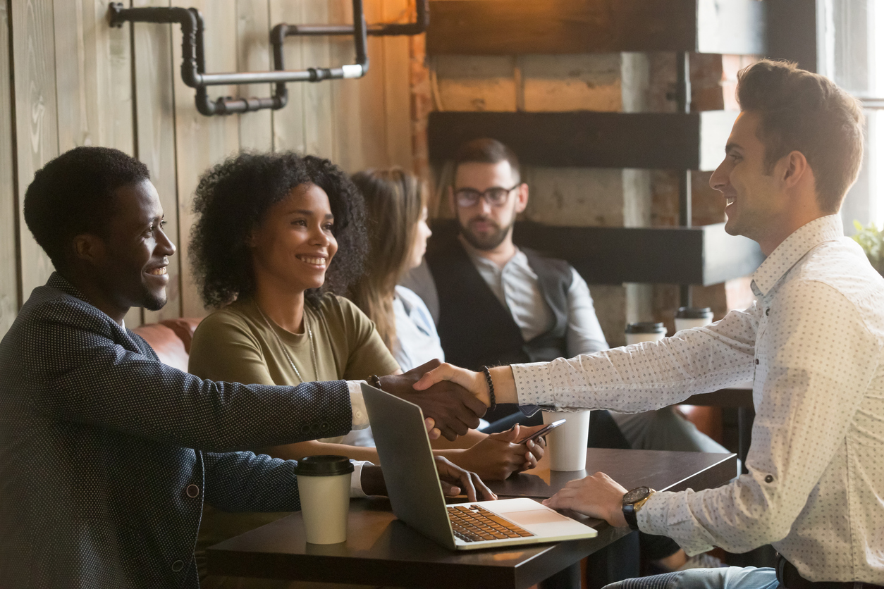 Multiracial african and caucasian men handshaking at meeting in cafe, diverse friends greeting sitting at coffeeshop table or black couple making deal shaking hands to white businessman with laptop. concept: Microloans vs the 3 F's