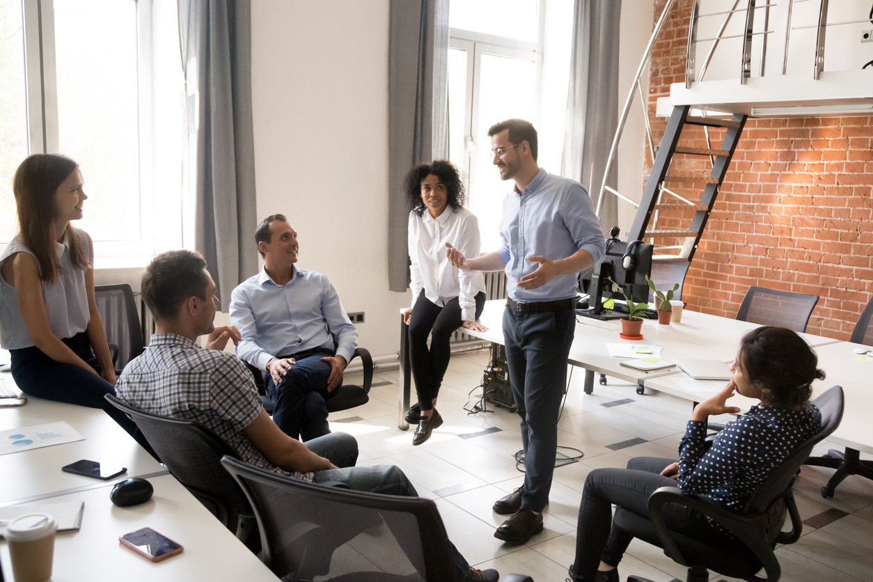 Confident business coach talking with multiracial group of office workers, having good conversation with subordinate, brainstorming, discussing business strategy, ideas, team building activity