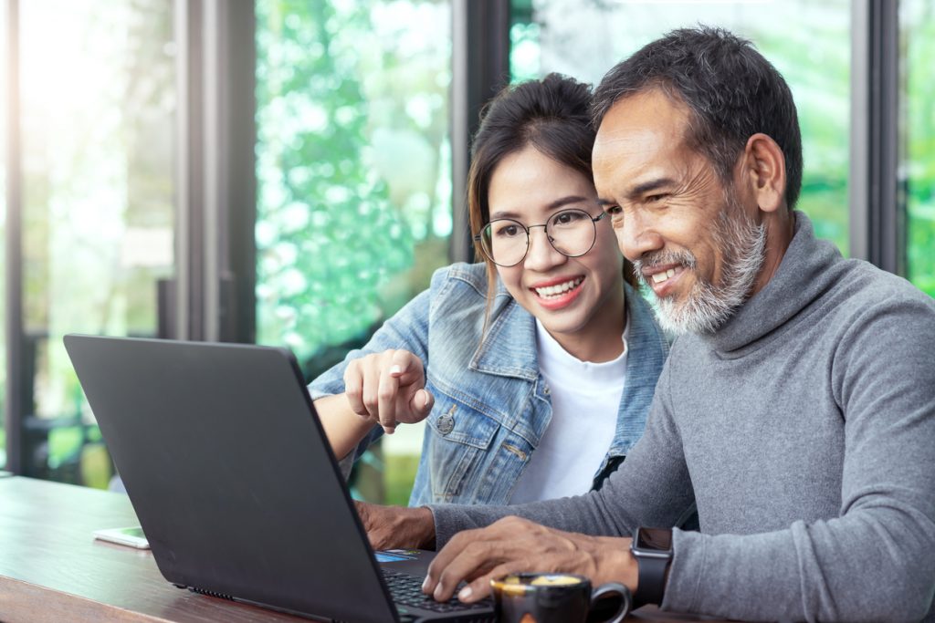 Hombre mayor y chica joven mirando computadora, joven enseñándo sobre computación a hombre mayor. concept: Roth IRA