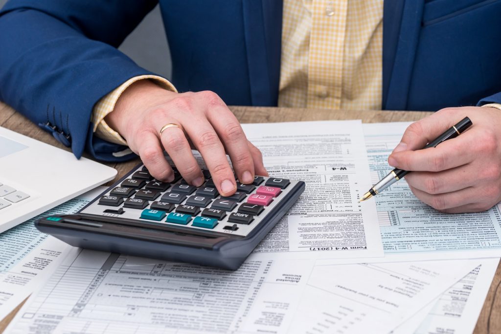Hombre haciendo su declaración de impuestos, hojas, papeleo, calculadora. Concept: software de impuestos